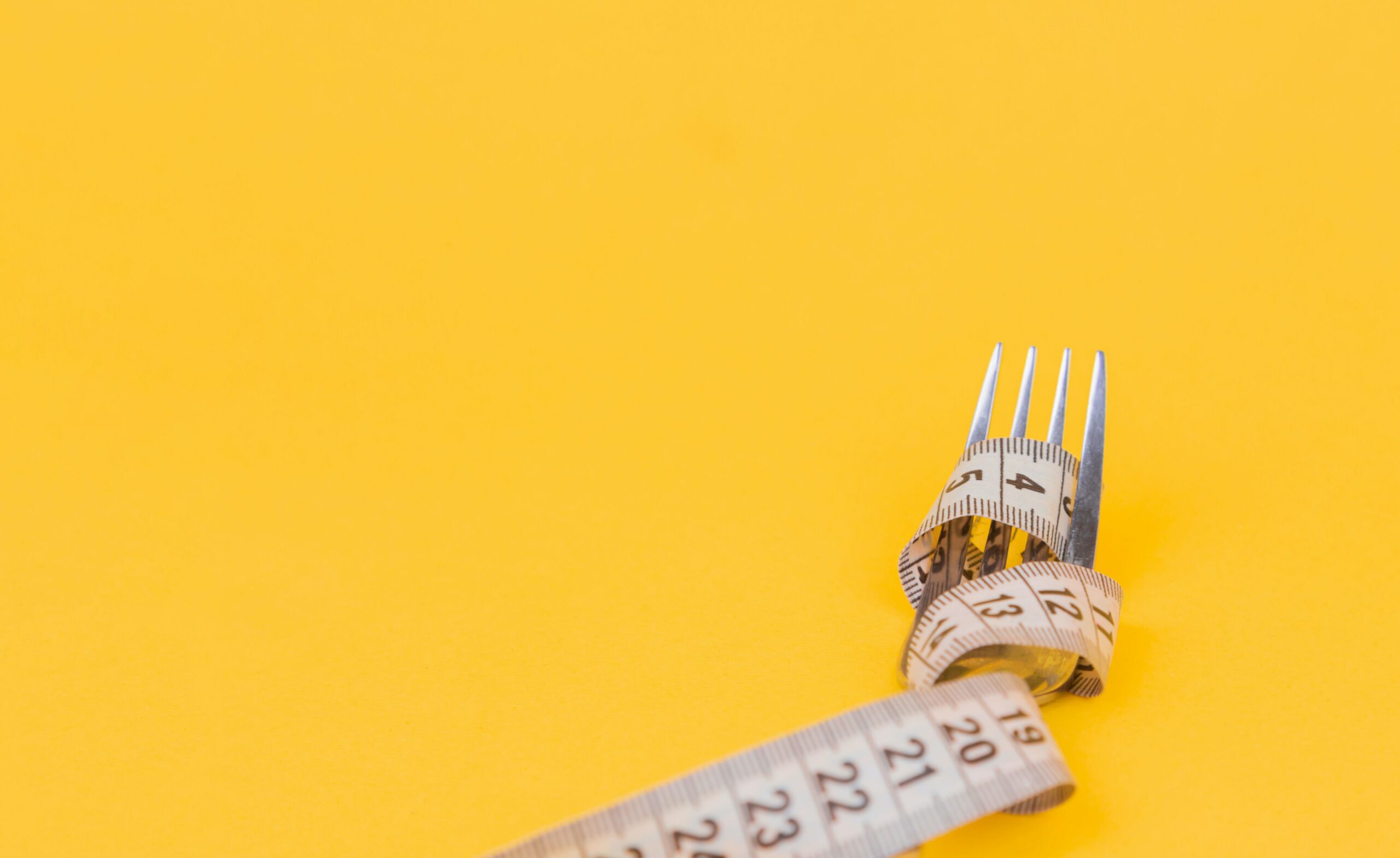Fork with measuring tap wrapped around it on a yellow background